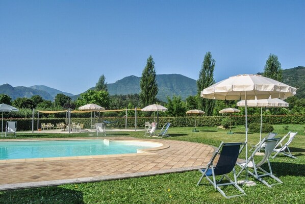 A pool area with lounge chairs and umbrellas, surrounded by greenery and mountains. - Houses in Stratola - Apartment 2 (Montella)