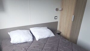 A bed with a grey quilt, a wooden headboard, and a white wall. - Mobile home Mimizan (Mimizan)