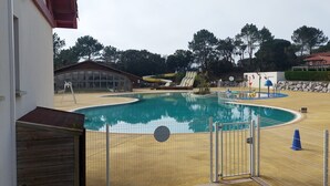 A swimming pool with a fenced area, a covered structure, and a building with a red roof. - Mobile home Mimizan (Mimizan)