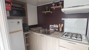 A compact kitchenette with a gas stove, a sink, and a microwave. There are wooden cabinets and a small shelf with kitchen utensils. - Mobile home Mimizan (Mimizan)