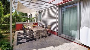 Une terrasse couverte avec une table et des chaises, une porte vitrée et un mur rouge.