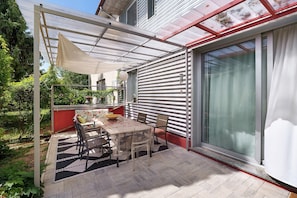 A covered patio with a table and chairs, a glass door, and a red wall.