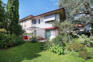 A two-story house with a red awning, a patio with outdoor furniture, and a well-maintained garden.