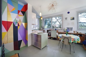 A kitchen with a colorful geometric wall, a dining table with chairs, and a view through large windows.