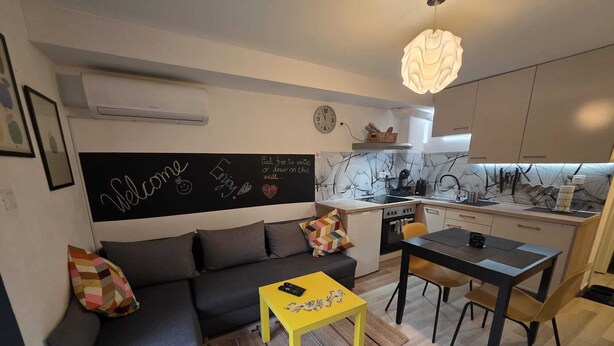 A compact living space with a sofa, a small dining table, a kitchen area, and a wall-mounted air conditioner. - City Oasis with Garden, BBQ, Pet-Friendly, near city center (Zagreb)