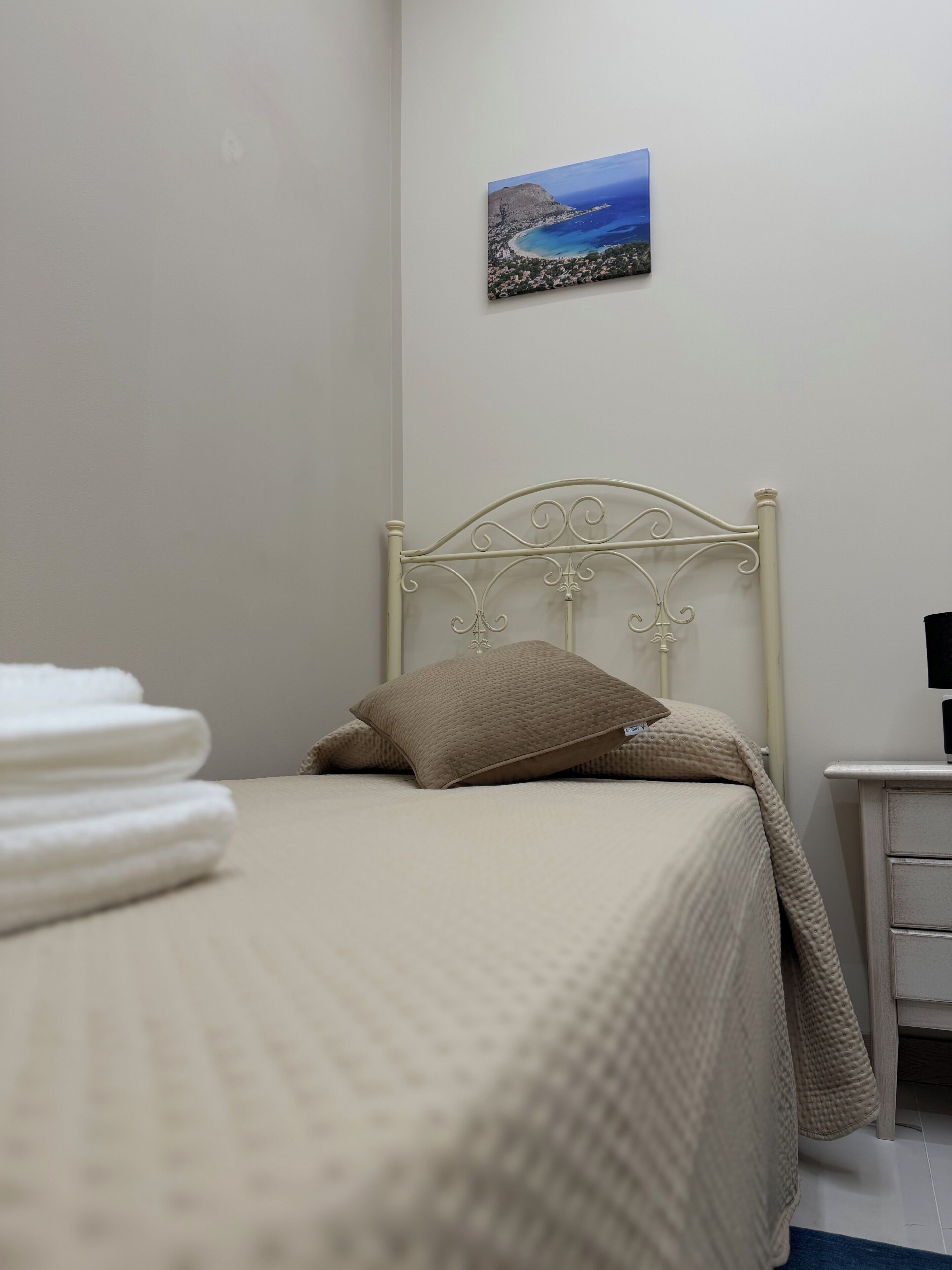 A neatly made bed with a headboard, a small bedside table, and a wall-mounted painting.