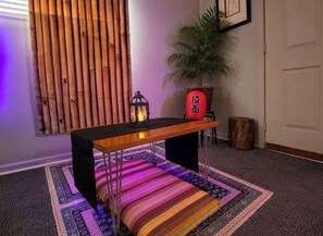 Una habitación con un panel de pared de listones de madera, una mesa negra con un banco, una planta en maceta y un farol.