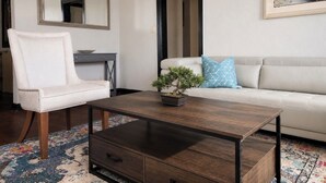 Ein Wohnzimmer mit einem weißen Sofa, einem weißen Sessel, einem dunkelholzboden-Couchtisch, einer Topfpflanze und einem Gemälde von Booten.