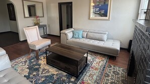 Ein Wohnzimmer mit Deckenventilator, einer Couch, einem Sessel, einem Couchtisch und einem gemusterten Teppich.