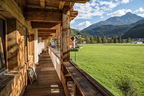 Een houten gebouw met een overdekte veranda, een grasveld en bergen op de achtergrond.