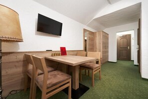 Una habitación con una mesa y sillas de madera, un televisor montado en la pared y un piso cubierto de alfombra verde.