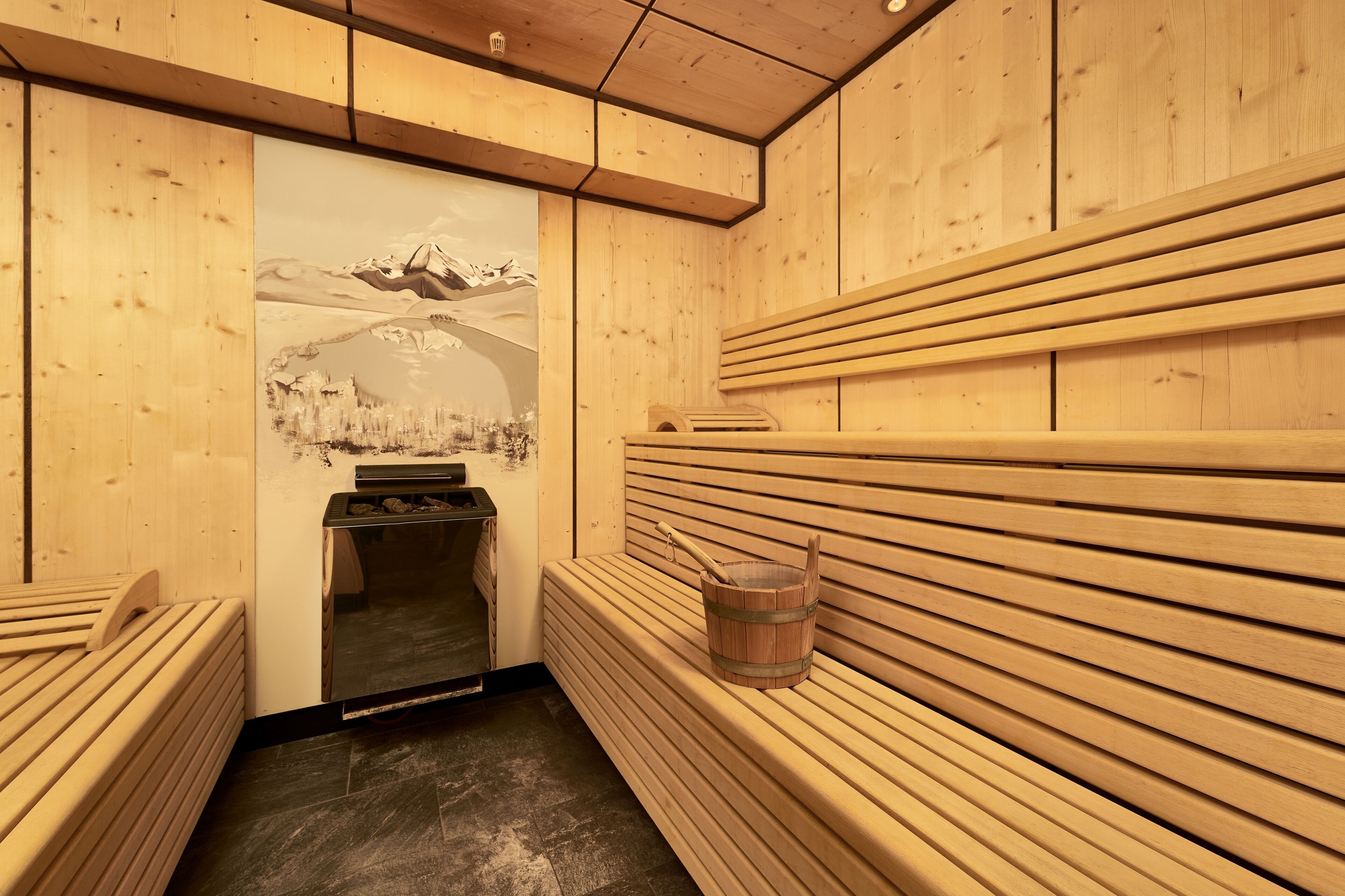 A sauna with wooden benches and a wooden bucket.