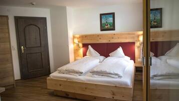 Een houten bed met witte beddengoed, een houten hoofdbord en een deur met een afbeelding erboven.