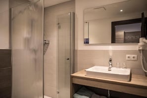 Un baño moderno con cabina de ducha de vidrio, un lavamanos con espejo y un perchero debajo.
