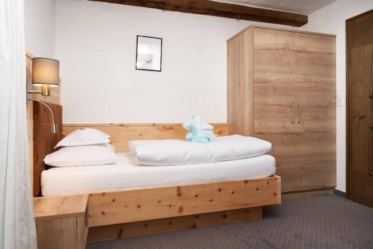 A single bed with a wooden headboard, a nightstand with a lamp, a large wardrobe, and a framed picture on the wall.