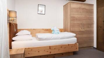 A single bed with a wooden headboard, a nightstand with a lamp, a large wardrobe, and a framed picture on the wall.