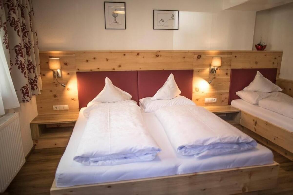 A room with two single beds, wooden headboards, wall-mounted lamps, and framed pictures on the wall.