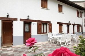 A building with white walls, wooden shutters, and a tiled patio with white furniture. - Apartamentos Irati Olaldea (Oroz Betelu)