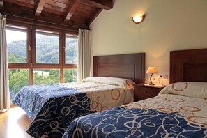 A room with two beds, a wooden ceiling, a nightstand with a lamp, and a window with a view of greenery. - Apartamentos Irati Olaldea (Oroz Betelu)