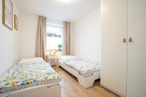 Ein Schlafzimmer mit zwei Betten, einem Schreibtisch, einem Fenster mit Vorhängen und einem Kleiderschrank.