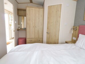 A bedroom with a bed, two wooden wardrobes, a small bedside table, and a mirror. - Caravan A7 (Bridport)