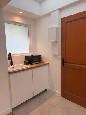 Eine kleine Küche mit Fenster, einer Mikrowelle und einem Spülbecken.
