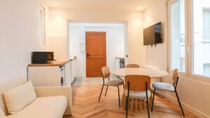 Un espacio habitable compacto con zona de comedor, sofá, televisor montado en la pared y una puerta de madera.
