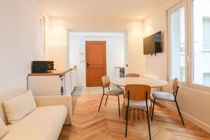 Ein kompakter Wohnbereich mit Essplatz, einer Couch, einem an der Wand befestigten Fernseher und einer Holztür.