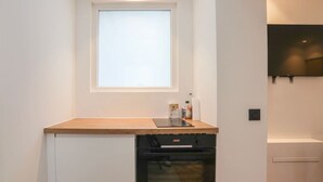 Una cocina compacta con horno integrado, una ventana sobre la encimera y un televisor montado en la pared.