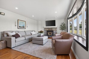 Un salon moderne avec une cheminée, un canapé, un pouf et une grande fenêtre.