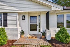 A white house with a front door, a 'hello' mat, and two potted plants.