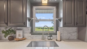 A kitchen with a window, a sink, cabinets, a plant, and a book on the counter. - Hot Tub Farm Home, Near Sight & Sound (Ronks)