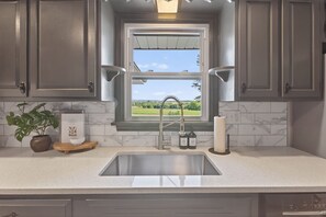 A kitchen with a window, a sink, cabinets, a plant, and a book on the counter.