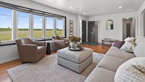 A spacious living room with a large window, a sofa, a chair, and a decorative ottoman. - Hot Tub Farm Home, Near Sight & Sound (Ronks)