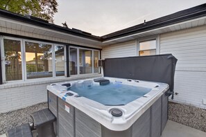 A hot tub in a covered outdoor area with a brick wall and windows.
