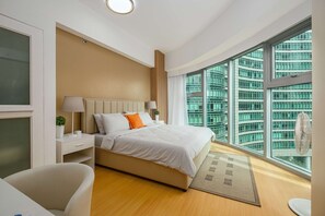A modern hotel room with a large bed, a desk, a chair, and a view of a high-rise building. - Modern Luxe Stay-2BR City Escape (Taguig City)