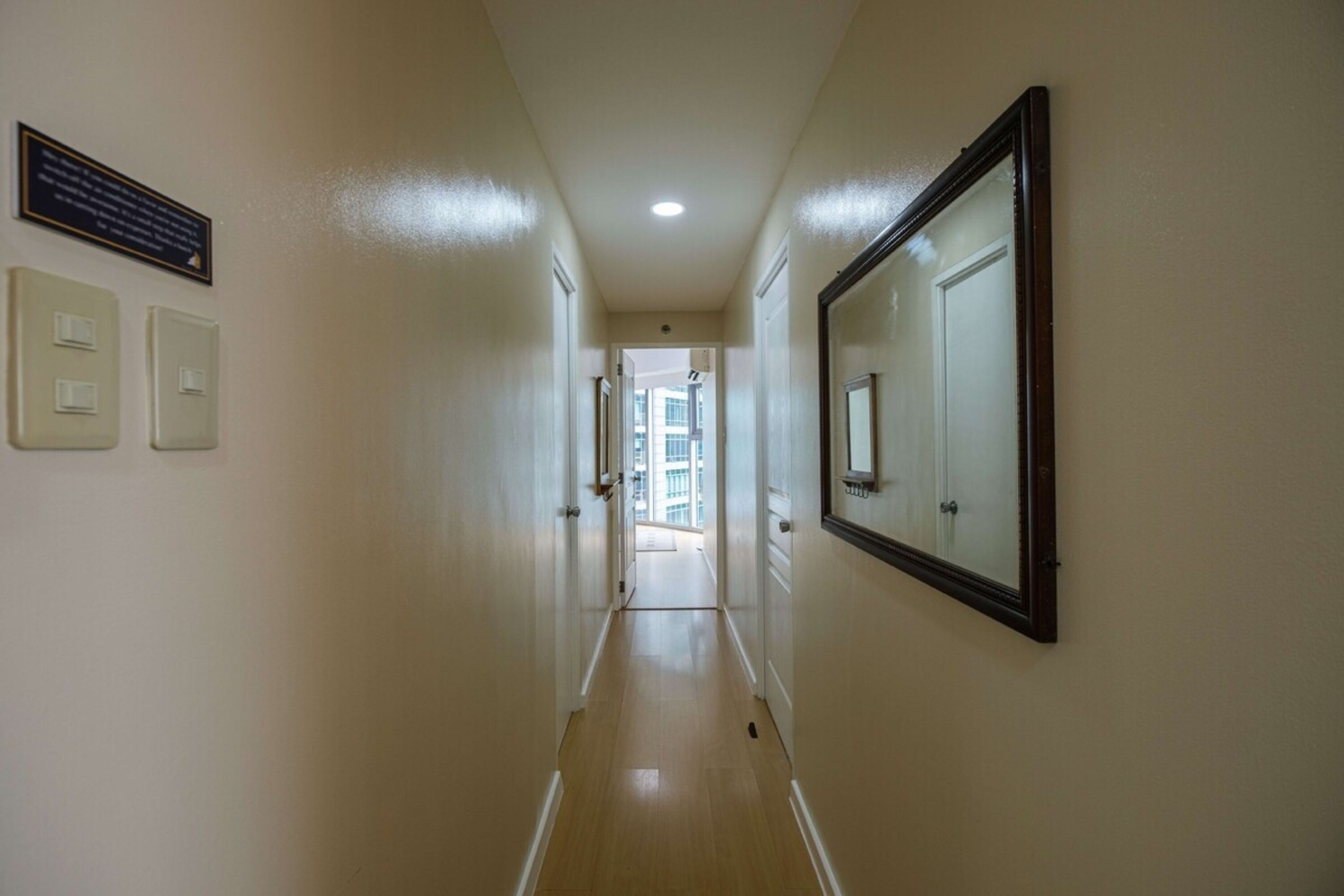 Un couloir aux murs de couleur claire, avec un plancher en bois, un grand miroir et une porte donnant sur un balcon.