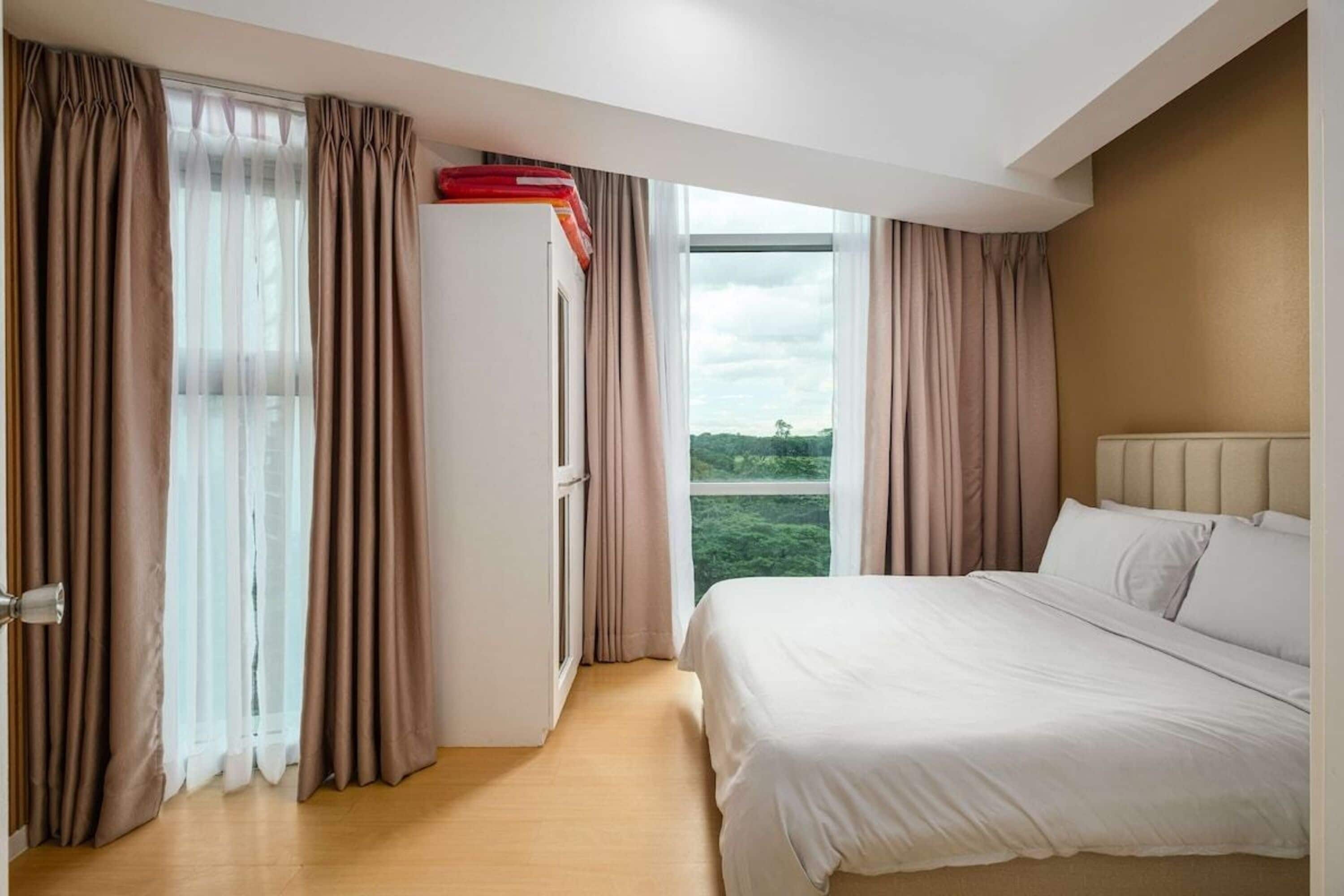 Une chambre d’hôtel avec un grand lit, une fenêtre avec des rideaux, une porte et une vue sur la verdure à l’extérieur.