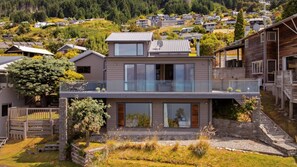 Ein modernes, zweistöckiges Haus mit Balkon, einer Steinmauer und Blick auf eine Wohngegend.