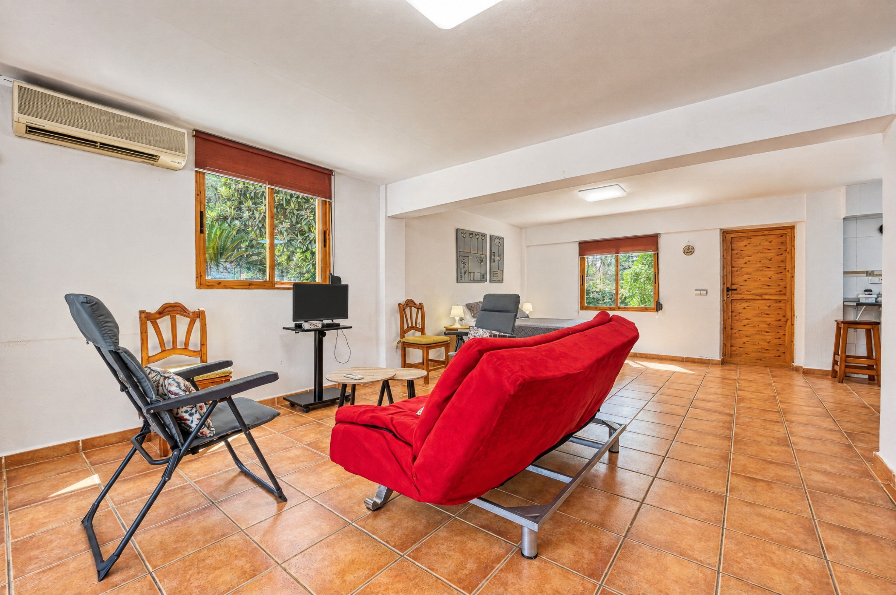 A spacious room with a red chair, a TV, and a dining area.