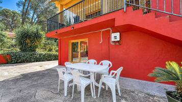 Un edificio rojo con un balcón, una mesa blanca con sillas y una planta en maceta.