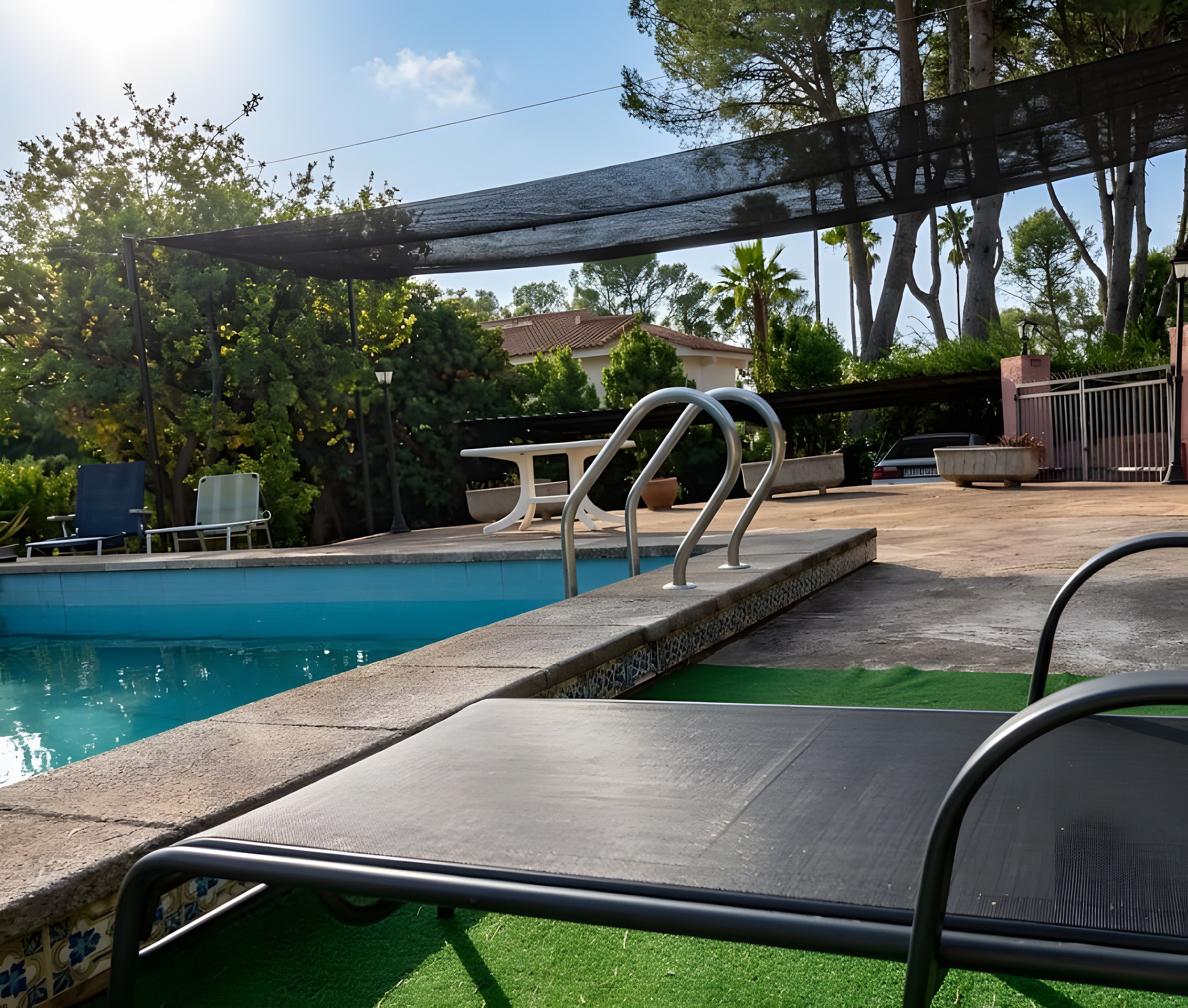 Una piscina con una escalera de metal, una zona de estar cubierta y una vista de un edificio al fondo.