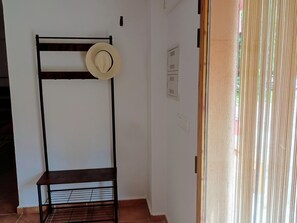 Ein Zimmer mit einer Metallregaleinheit, einem daran hängenden Hut und einem Fenster mit vertikalen Rollläden.