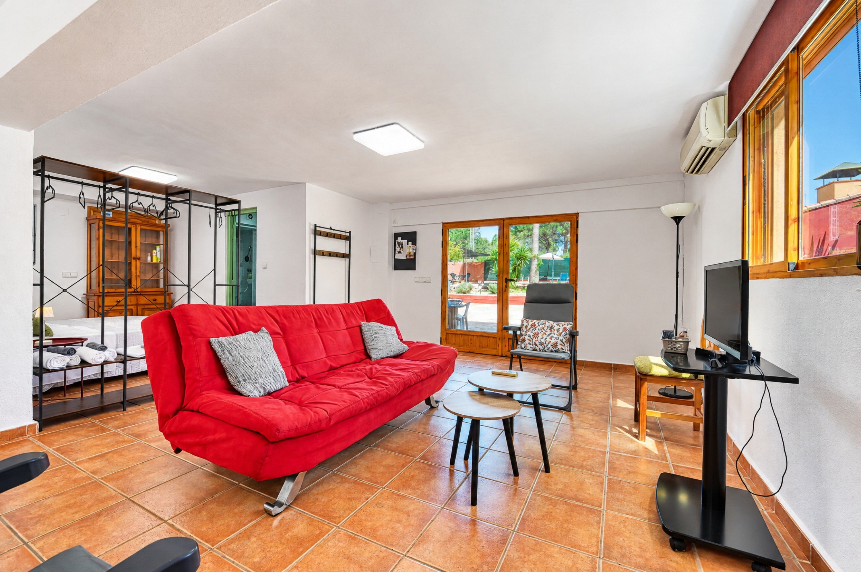 A living room with a red sofa, a small table, a TV, and a view of the outside.