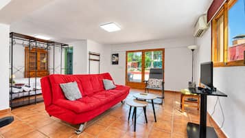 A living room with a red sofa, a small table, a TV, and a view of the outside.