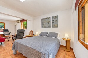 A bedroom with a bed, two bedside tables, a chair, a desk, and a window.