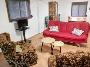 Un salon avec un canapé rouge, des fauteuils à motifs, un téléviseur et un meuble.