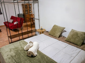 Une piÚce comprenant un lit, un canapé rouge, une armoire en bois et une petite table ronde.