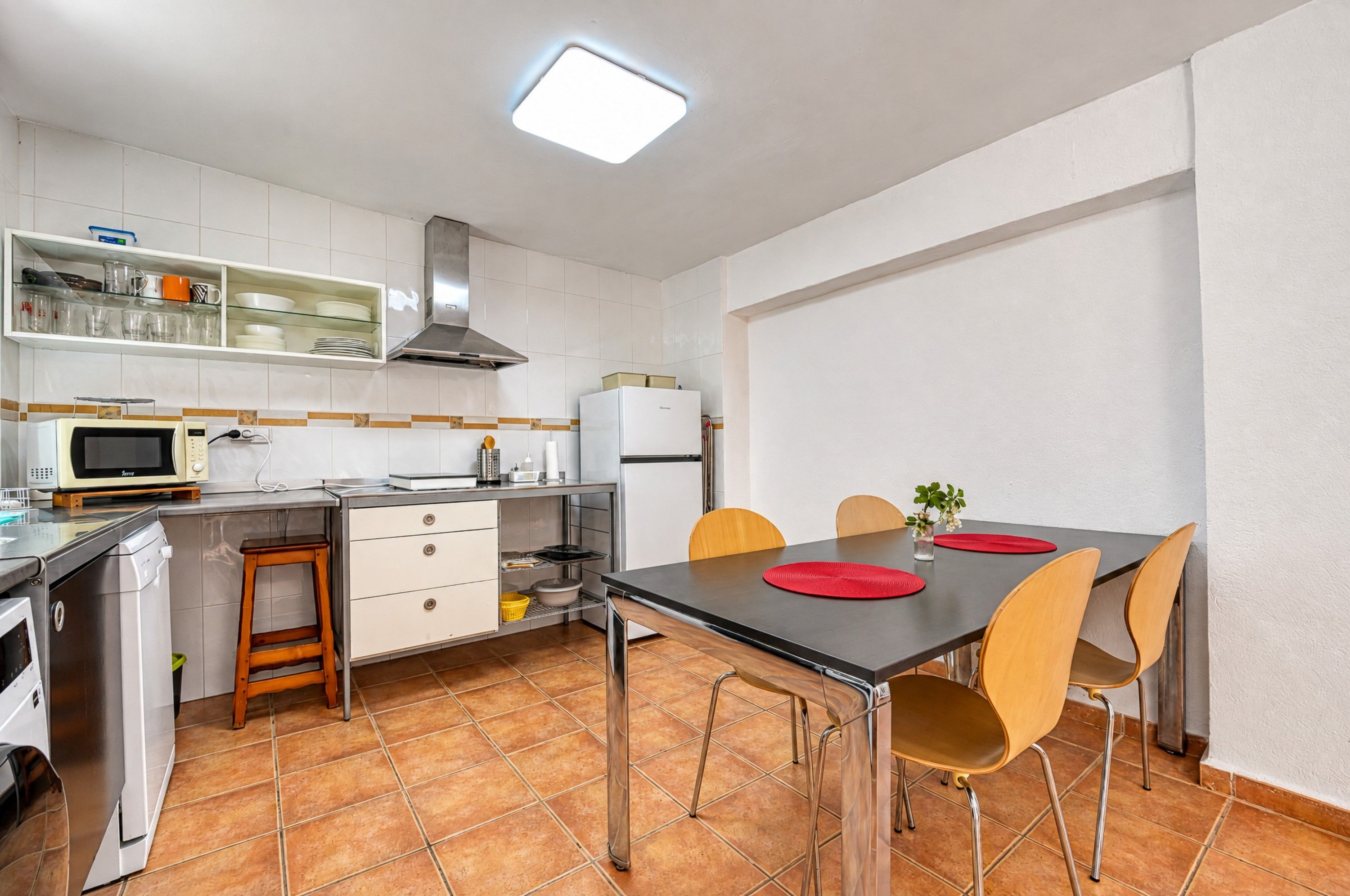 Una cocina compacta con armarios blancos, un microondas, una estufa y una mesa de comedor con sillas.