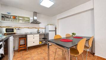 Una cocina compacta con armarios blancos, un microondas, una estufa y una mesa de comedor con sillas.